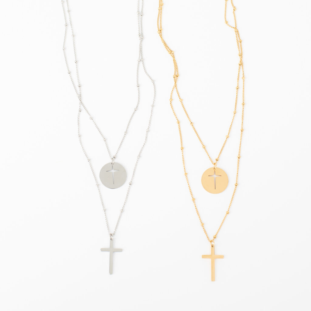 Gold and silver Blessing layered necklaces with cutout cross discs and longer cross pendants on a white background.