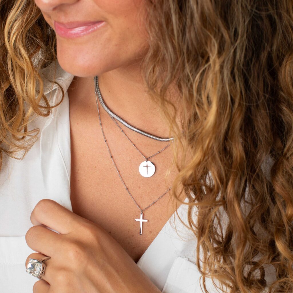 Woman wearing the silver Blessing layered necklace with a cutout cross disc and longer cross pendant, styled with a textured silver chain and white blouse.