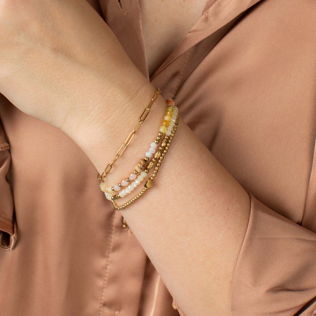 Gold Liza and Florence bracelets layered together on a wrist, combining colorful faceted beads, paperclip chain, polished gold beads, and a small heart accent.