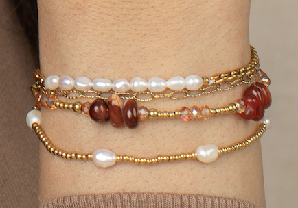 Model wearing a coordinated bracelet stack with freshwater pearls, gold metal beads, chain details, and warm carnelian stones.
