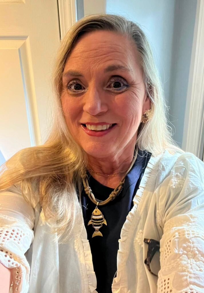 Woman wearing the Big Fish Charm on a knotted cord necklace with a navy top and white jacket.