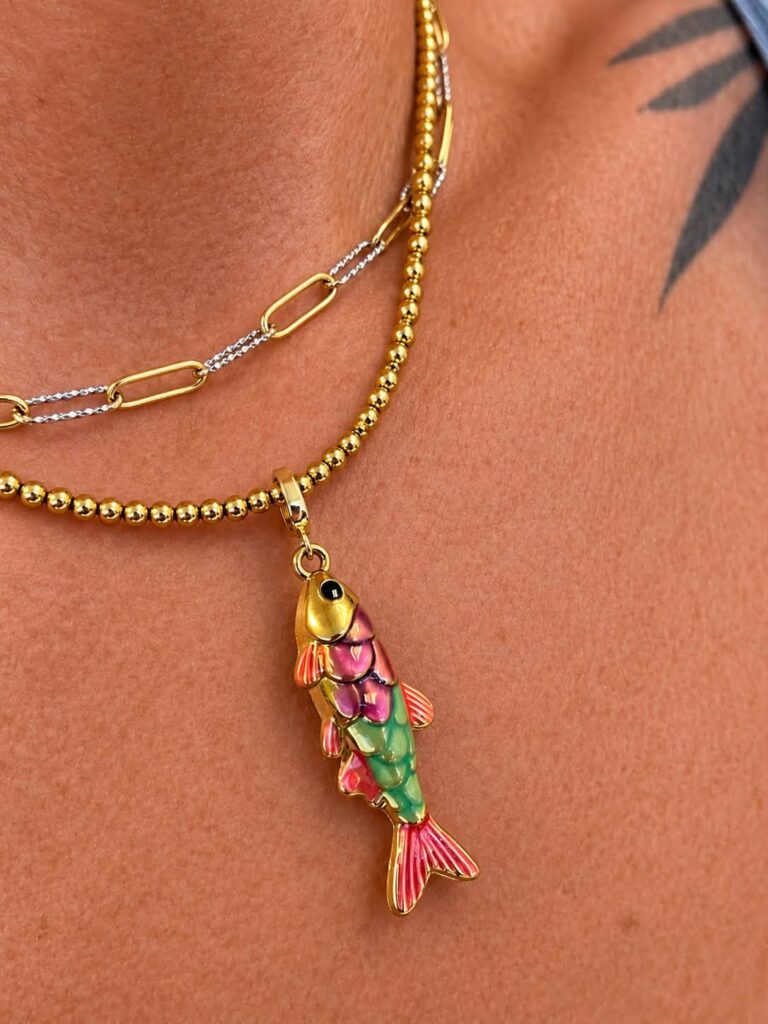 Colorful Rainbow Fish Charm worn on a layered gold necklace.