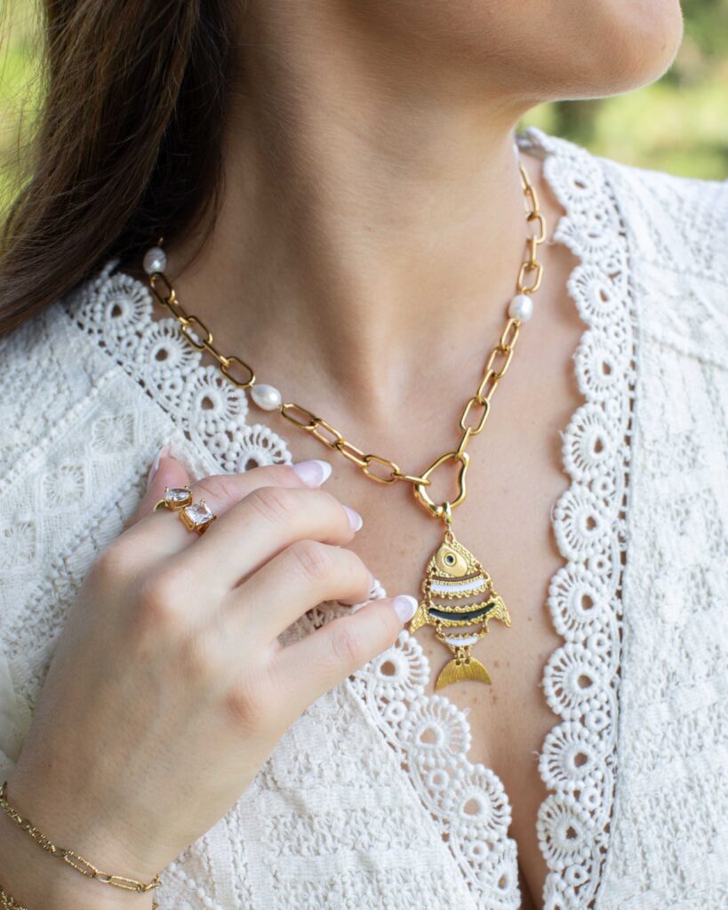 Big Fish Charm worn on a gold chain with pearl accents and a white lace top.