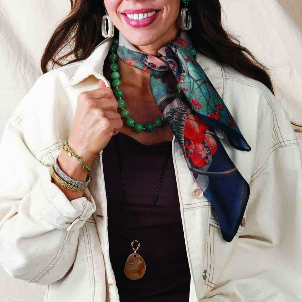 Model wearing the Briar chunky green beaded necklace with a colorful silk scarf, oversized silver earrings, a cream jacket, and a long pendant necklace. The bold green beads add a fresh pop of color while showing how oversized bead necklaces can be styled with scarves and layered accessories for Fall 2026.