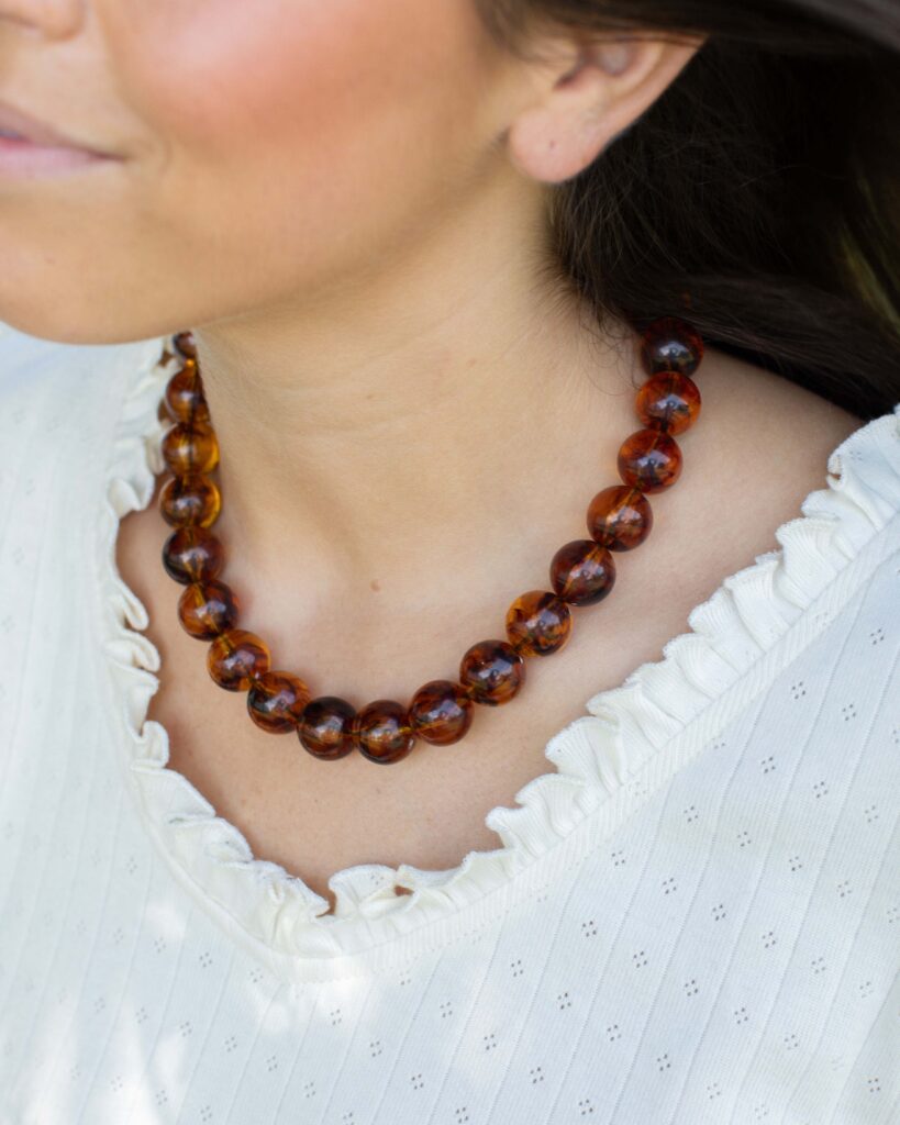 Woman wearing the Dinah amber marbled bead necklace with a white ruffle blouse, showcasing a bold resin statement necklace for fall styling.