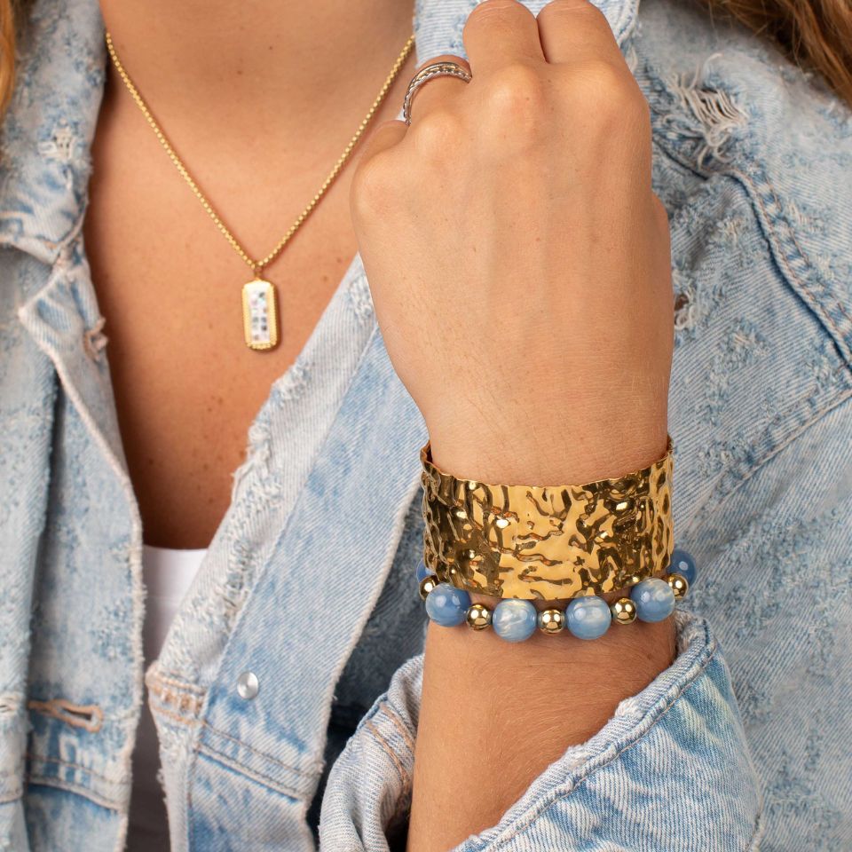 Elle hammered gold cuff styled with a blue beaded bracelet and a light-wash denim jacket.