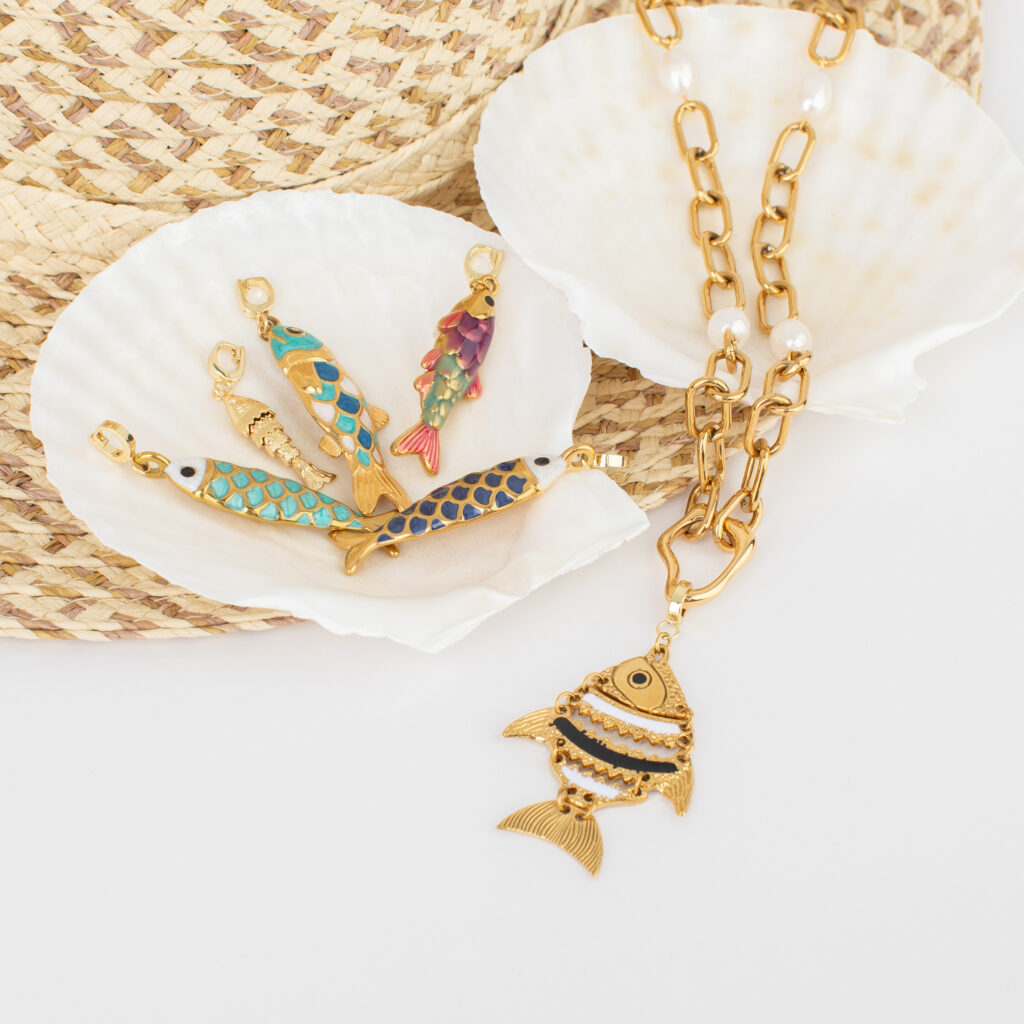 Gold fish charms and a chunky gold chain arranged on white shells and a woven straw background.