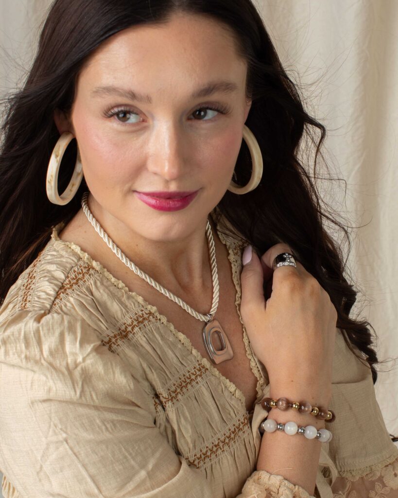 Woman styling the silver Louisa necklace with a neutral beige blouse, cream hoop earrings, and stacked bracelets.