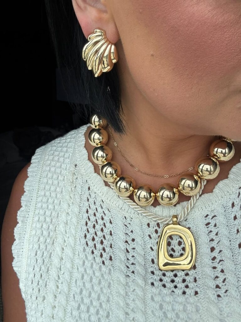 Gold Louisa cord necklace layered below a chunky gold bead necklace and delicate chain over a white crochet top.
