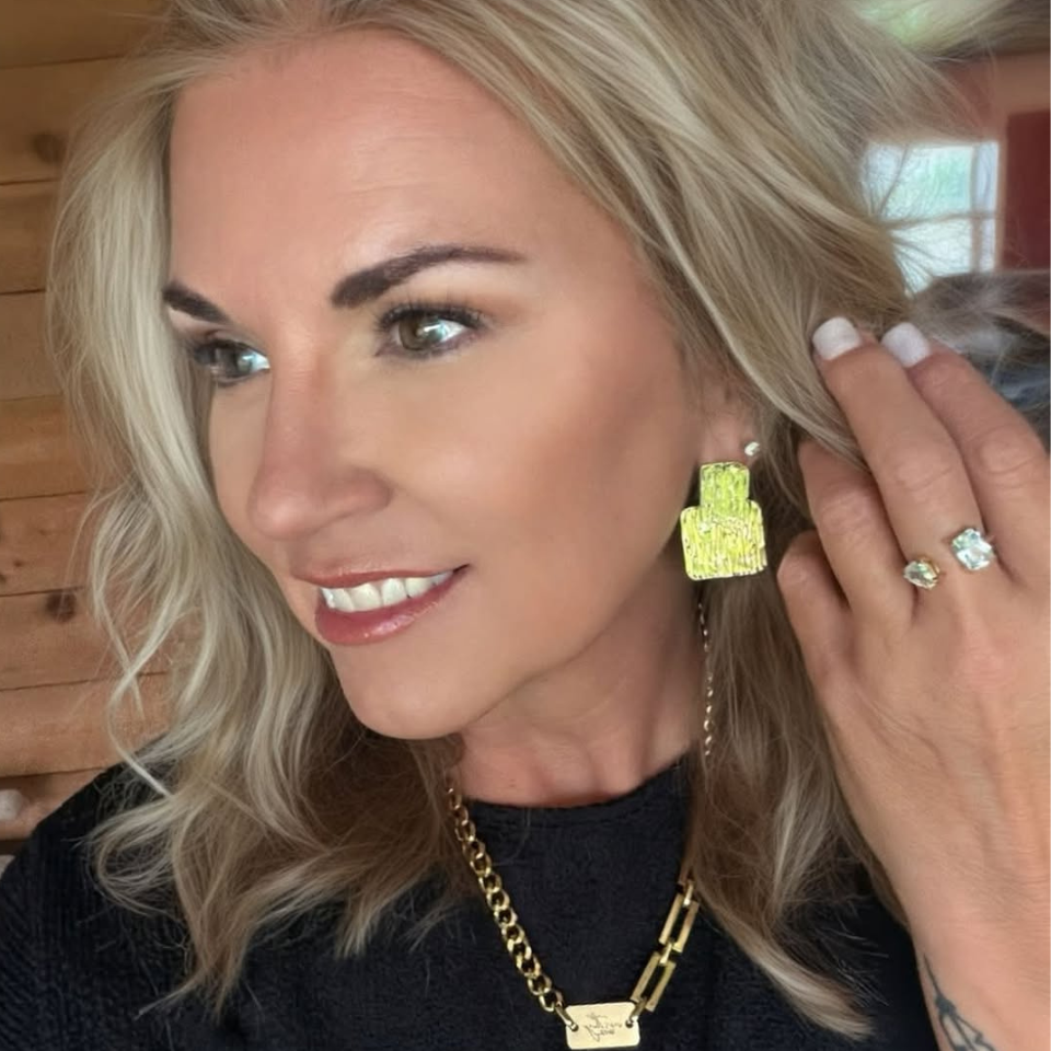 Woman in a black top wearing the textured geometric Margot gold statement earrings.