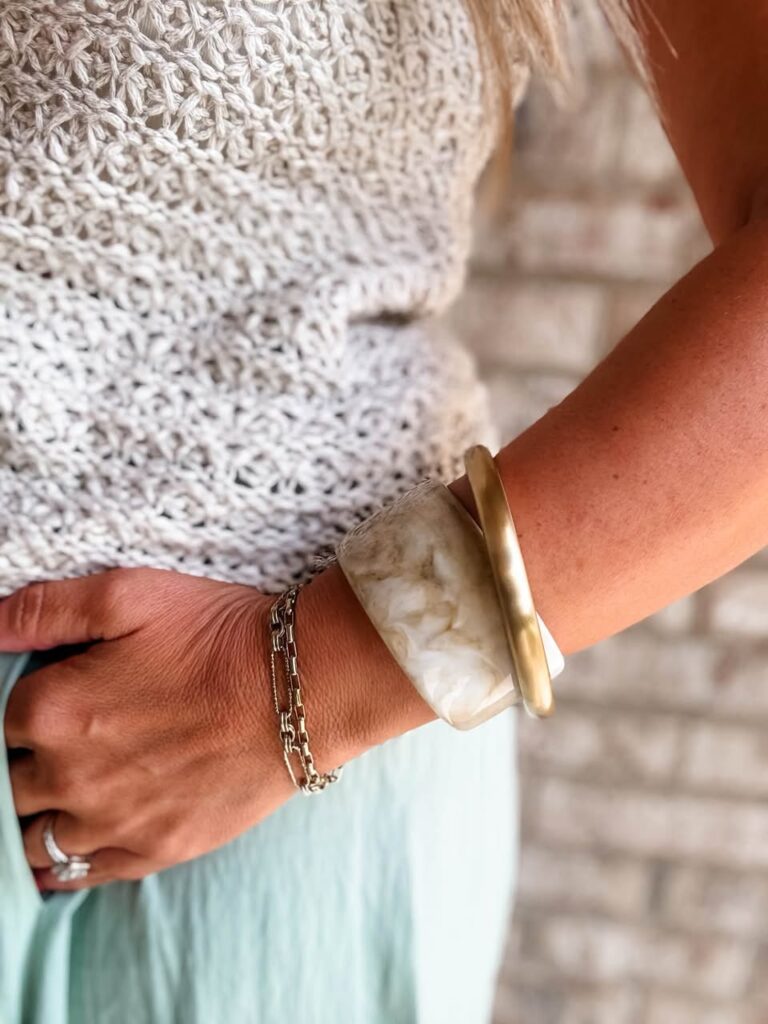 Cream marbled Julep resin cuff stacked with a gold bangle and delicate chain bracelets.