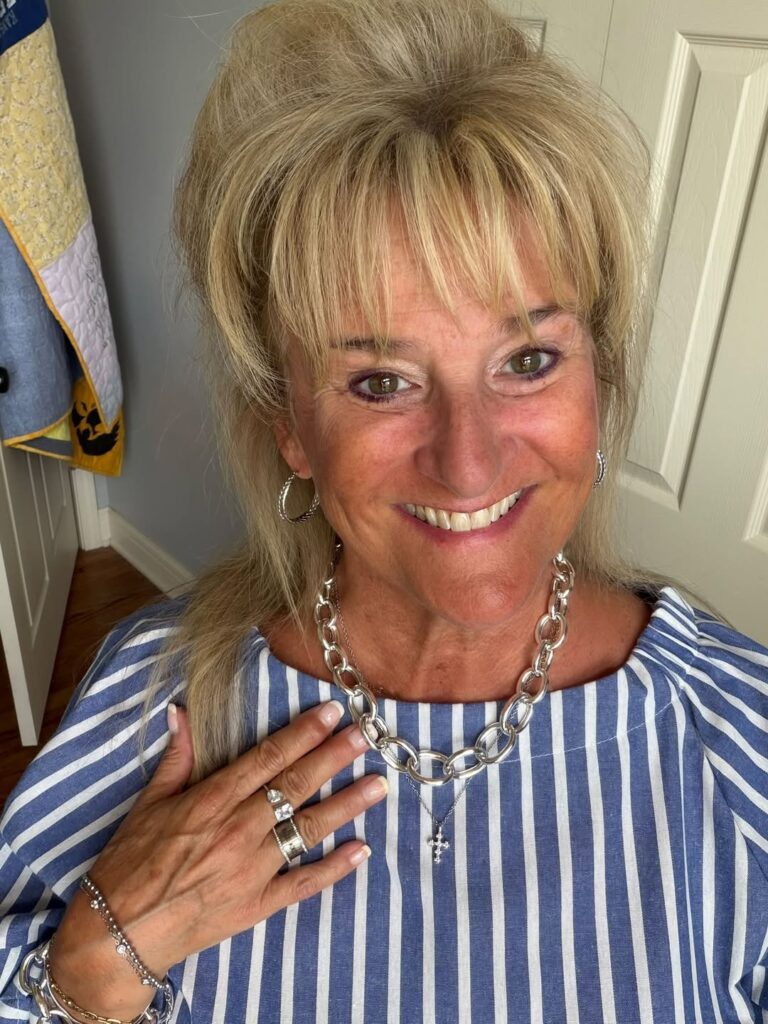 Woman wearing a bold silver link necklace layered with a delicate crystal cross necklace over a blue-and-white striped top.