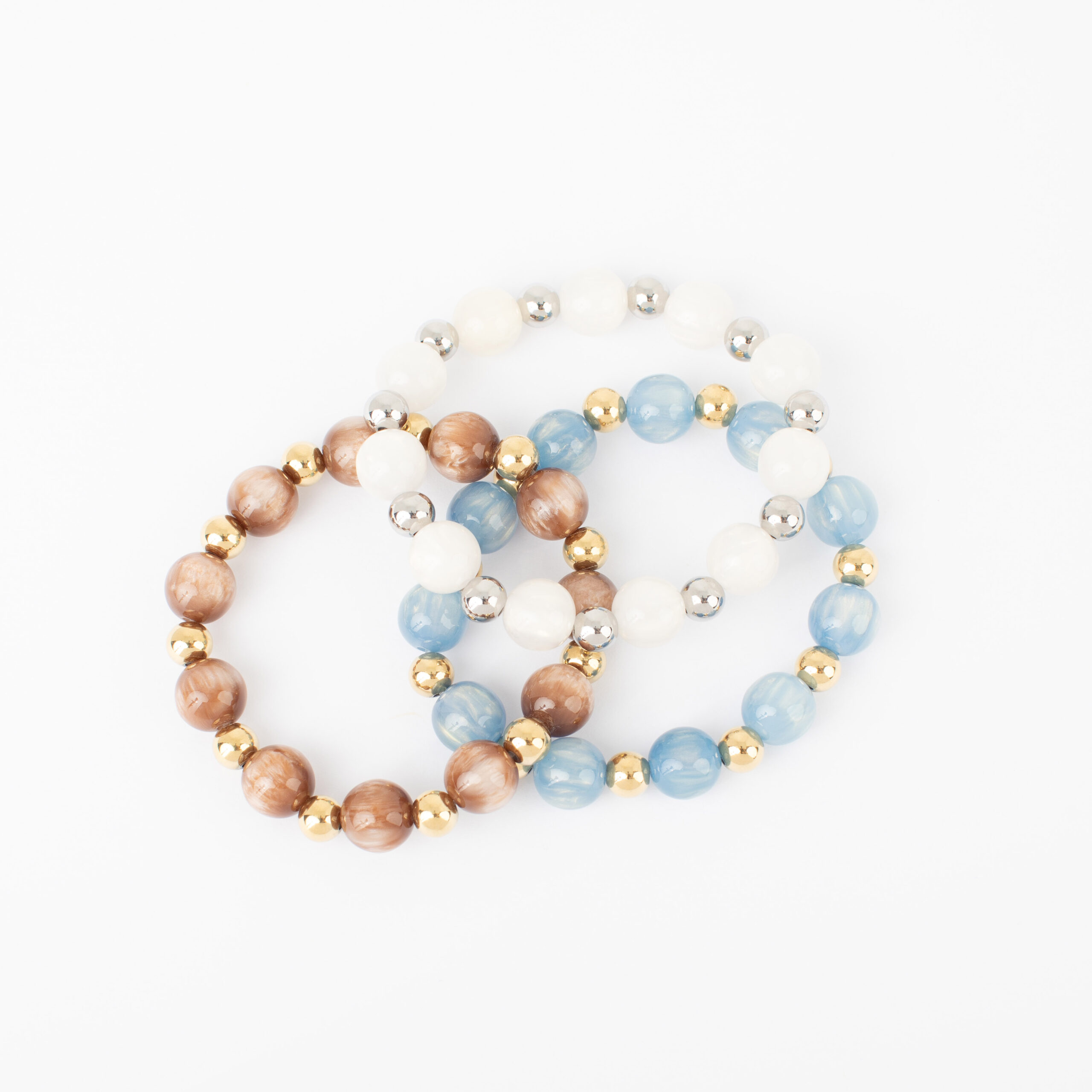 Three Fallon stretch bracelets featuring ivory, marbled brown, and dusty blue glass beads with polished gold- and silver-tone accents on a white background.