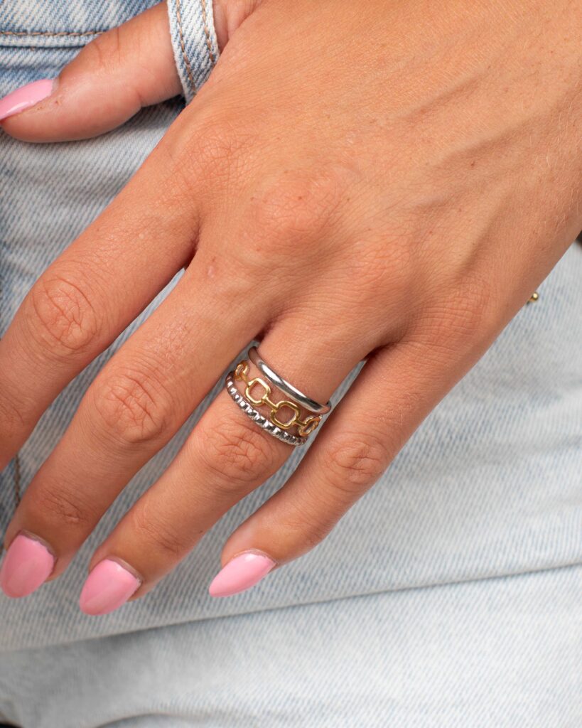 Close-up of the Janae mixed-metal ring worn on a hand with pink nails against light-wash denim. The ring features silver bands with a gold link-inspired center.