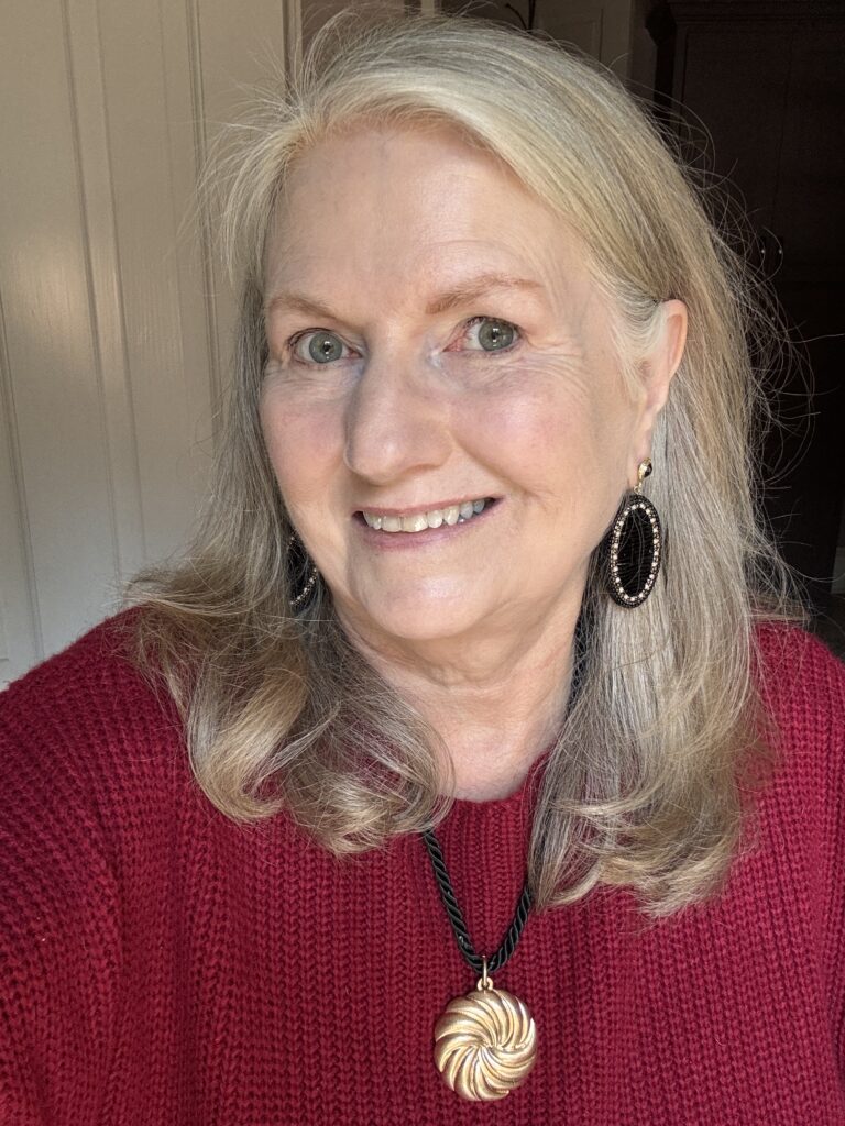 Audrey wearing the Ebony necklace, featuring a black twisted cord and round sculptural gold pendant, with a red textured sweater.
