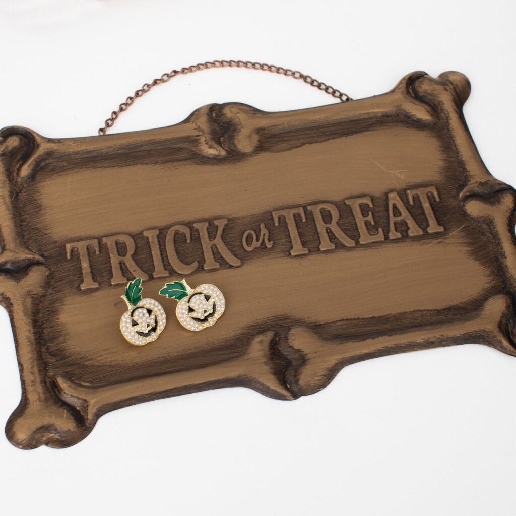 Pair of pearl jack-o’-lantern earrings displayed on a wooden Trick or Treat sign.