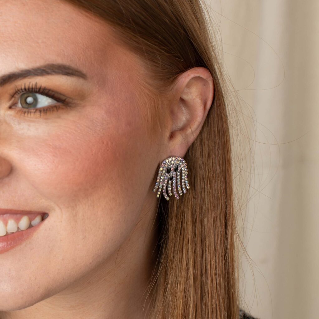 Woman wearing silver rhinestone ghost earrings with sparkling strands and black facial details.