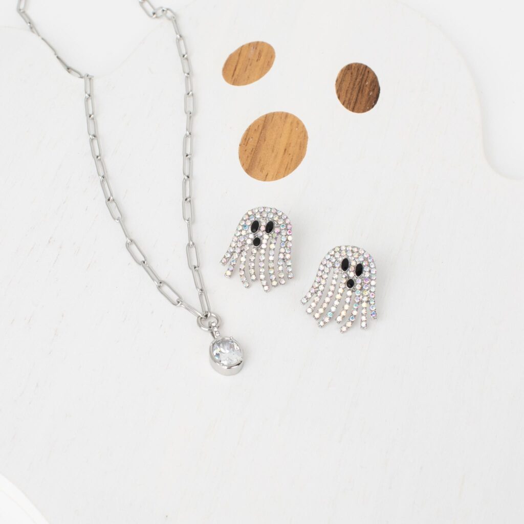 Silver Danielle Necklace with zircon pendant styled beside sparkling rhinestone ghost earrings on a white wooden ghost display.