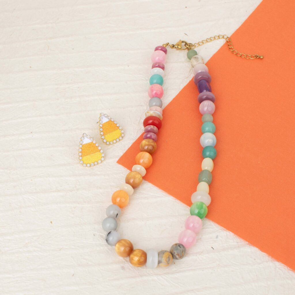 Orange and yellow candy corn earrings styled with the colorful beaded Justine Necklace on an orange-and-white background.