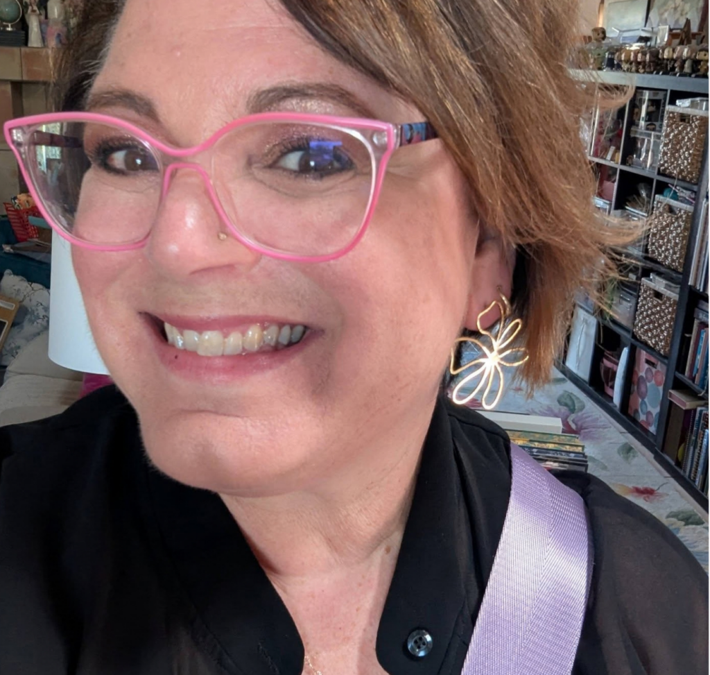 Woman in pink glasses and a black top wearing a gold Talia flower earring.