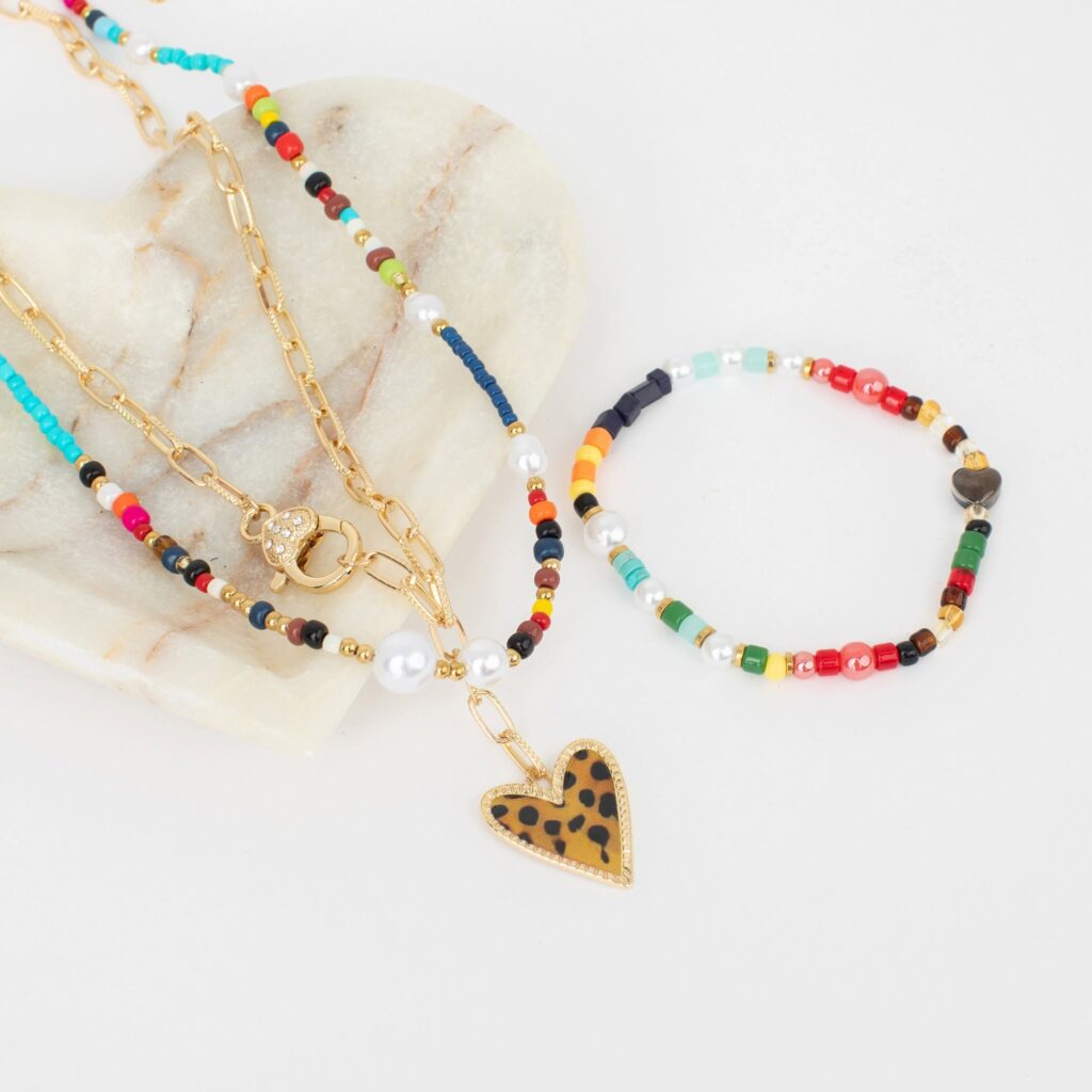 jBloom October Bloom Box jewelry: a gold-tone chain necklace with a leopard-print heart pendant, a colorful beaded necklace with pearl accents, and a multicolored beaded bracelet arranged beside a marble heart.