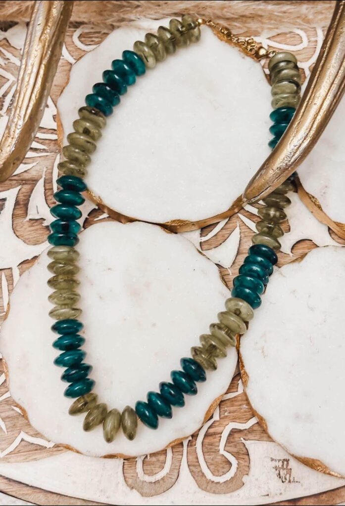 Cypress Necklace with evergreen and smoky neutral beads and a gold clasp, arranged on white and gold decorative tiles.