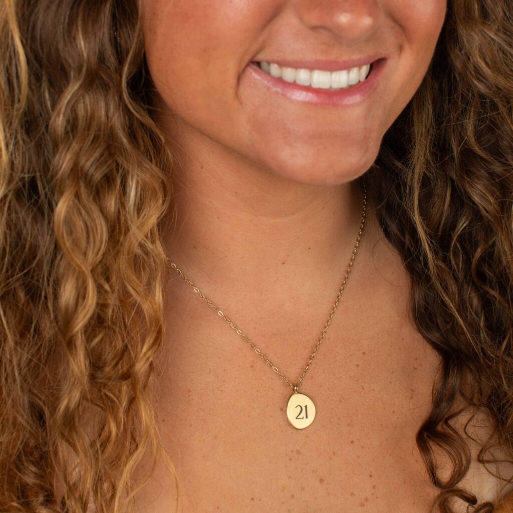 Woman wearing the gold Leya Necklace, featuring a delicate chain and a round pendant engraved with “21.”