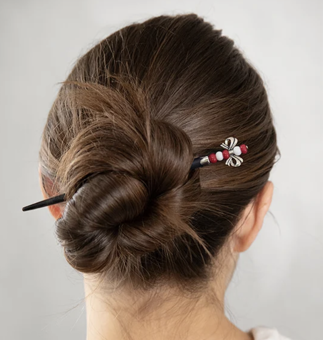 Rear view of a brunette updo secured with a black Festive Bow hair stick featuring red and white beads and a silver-tone bow.