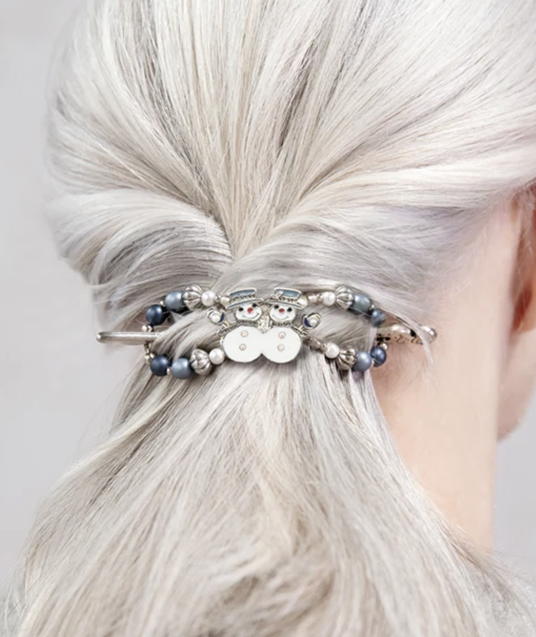 Silver hair in a half-up twist secured with a silver-tone hair clip featuring two smiling snowmen surrounded by blue, white, and silver beads.