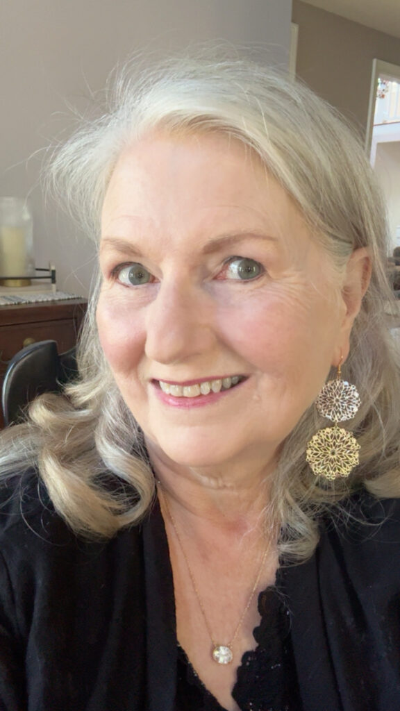 Audrey Peacock wearing Kara drop earrings with silver and gold lace-like circles, a black top, and a delicate pendant necklace.