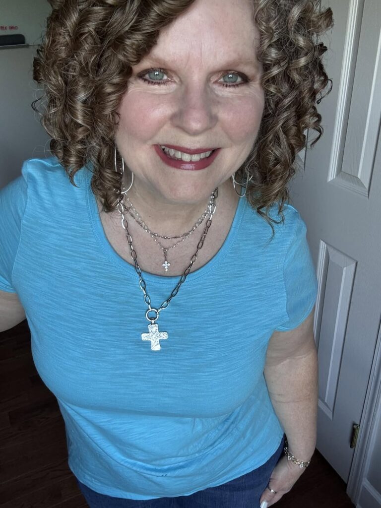 Woman wearing the Lora Necklace and Hammered Cross Charm with a blue top and separate layered necklaces