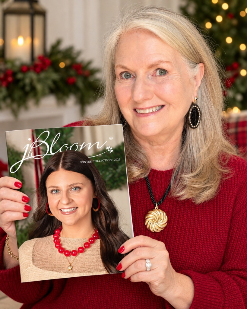 Alt text: Audrey smiles in a festive red sweater while holding the jBloom Winter Collection 2026 catalog, with holiday greenery, warm lights, and red accents in the background.