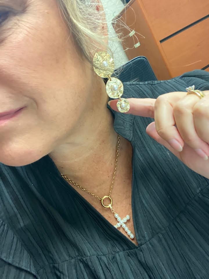 Close-up of a woman wearing Nicolette drop earrings with three textured gold-tone discs and pearl centers, alongside a pearl bow stud and layered necklaces.