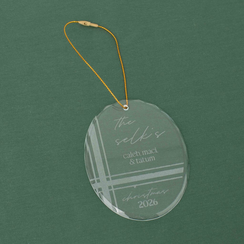 Clear oval glass ornament with engraved personalization and a gold hanging cord