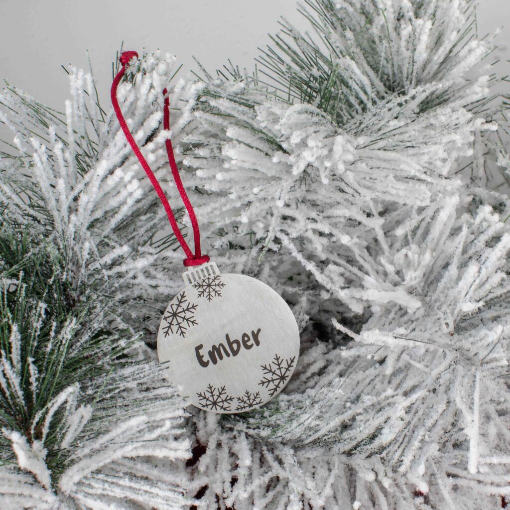 Small round ornament engraved with Ember and snowflakes on a flocked tree