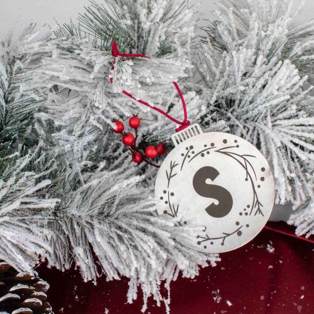 Round silver ornament with a large S initial hanging on a flocked tree